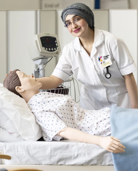Student gently supports a medical training mannequin while learning bedside care techniques. Student gently supports a medical training mannequin while learning bedside care techniques.